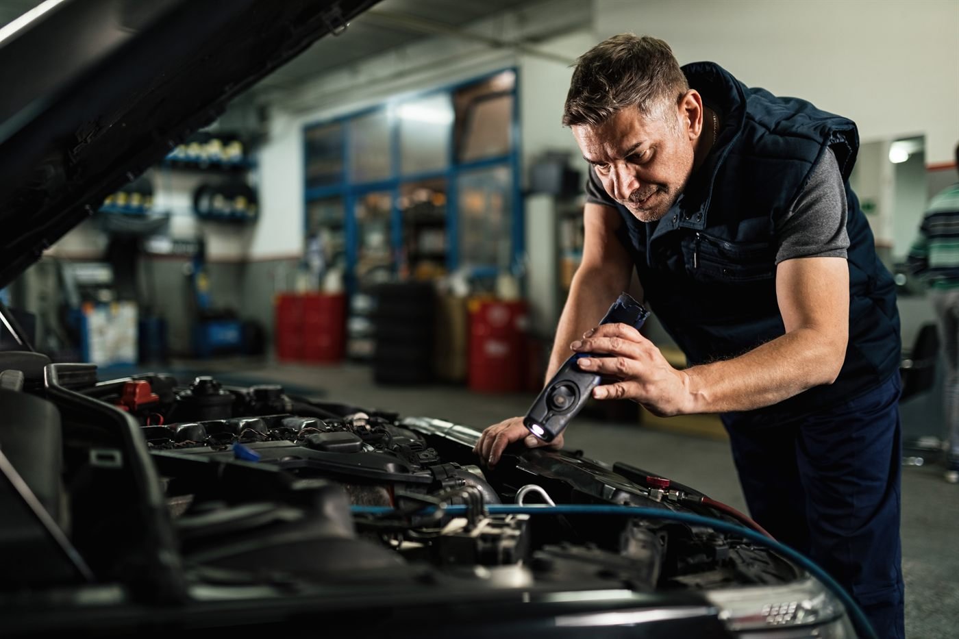 Técnico da Santa Cruz Imports inspecionando o motor de um veículo importado com lanterna